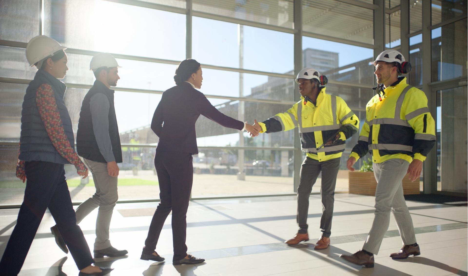 A group of people wearing suits shaking hands with construction professionals wearing PPE